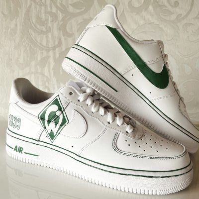 Weiße Nike Air Force 1 Sneakers mit grünem Logo und Details auf der Seite.