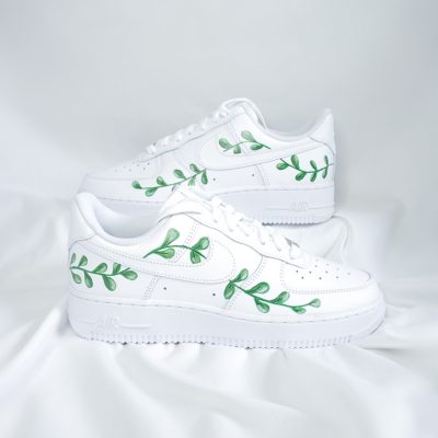 Weiße Nike Air Force 1 Sneakers mit grünen Blattmotiven auf der Seite, auf einem weißen Hintergrund.